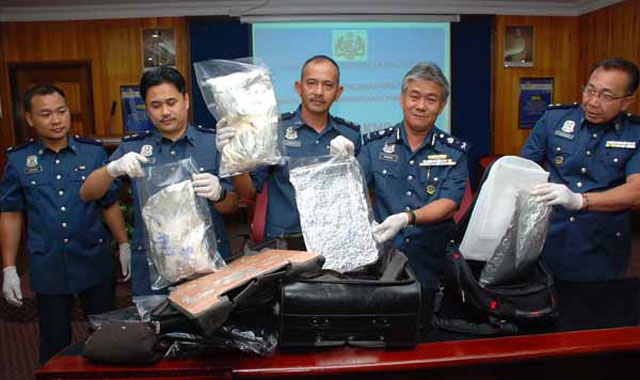 مأمورین مرزی و پلیس مالزی مواد مخدر گرفته شده از مسافرین را نشان می دهند. گویا از بسیاری از ایرانیان که همه روزه در مالزی به اتهام قاچاق دستگیر می شوند، شمار زیادی از آنها پس از بررسی تبرئه می گردند و بیگناه شناخته می شوند،